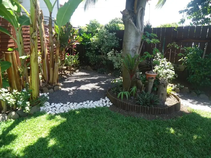 Un jardin luxuriant avec des plantes tropicales et une allée en gravier.