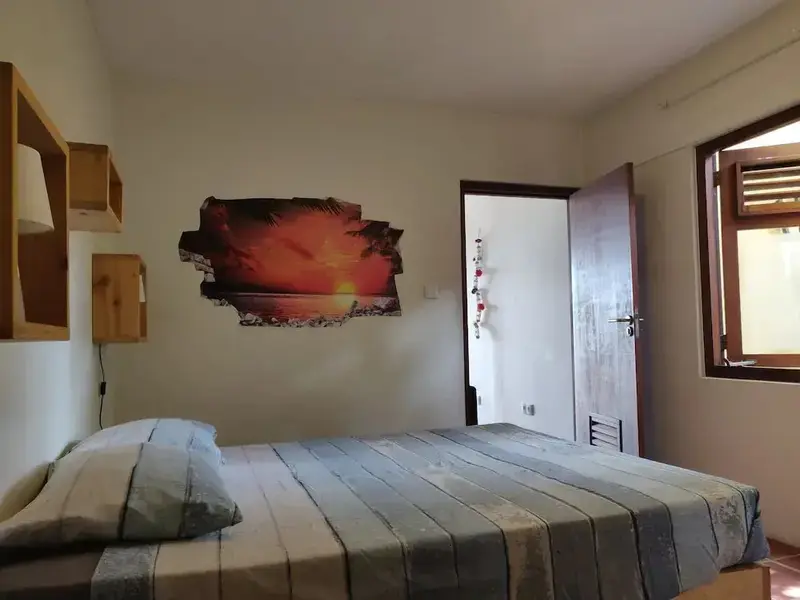 Une chambre lumineuse avec un lit simple et une décoration murale représentant un coucher de soleil.