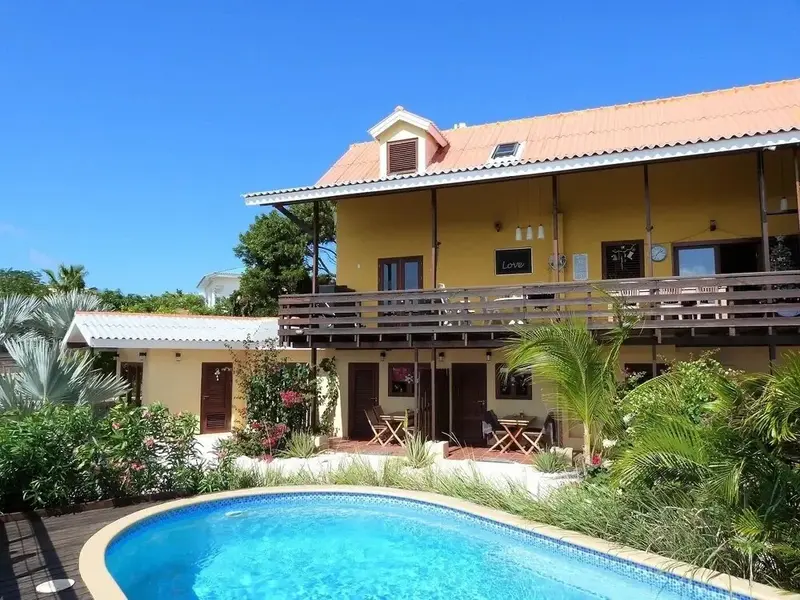 Bâtiment jaune à deux étages avec des balcons et une piscine au premier plan.