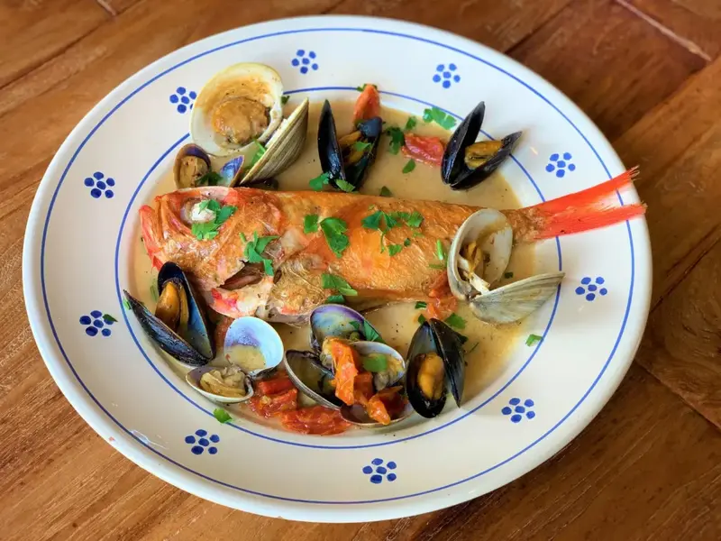 Un poisson entier servi avec des fruits de mer et une sauce crémeuse sur une assiette décorée.