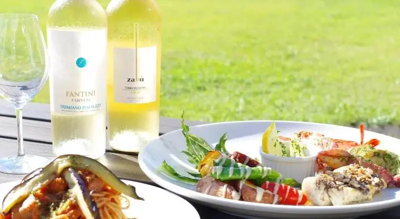 Assiettes de plats colorés et bouteilles de vin sur une table en extérieur.