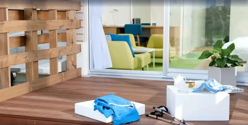 Terrasse en bois avec mobilier d'extérieur et vue sur un espace intérieur lumineux.