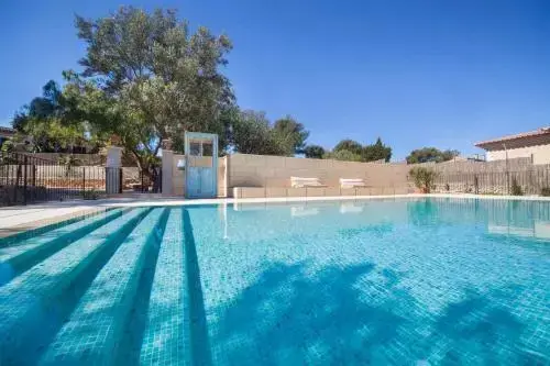Piscine rectangulaire entourée d'une terrasse ensoleillée et de végétation luxuriante.