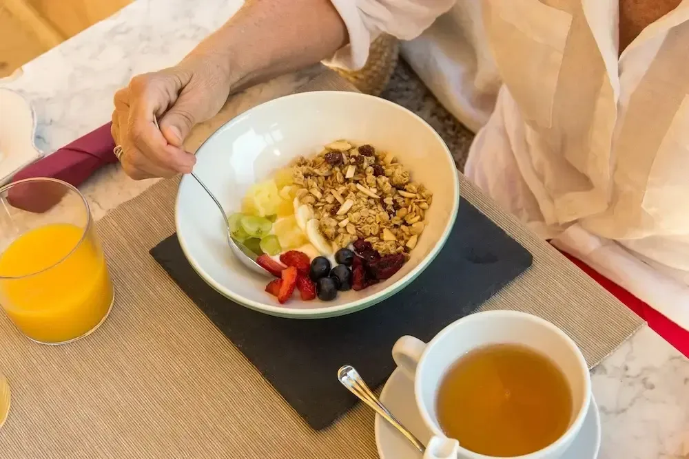 Un bol de fruits et de céréales est présenté sur une table avec une tasse de thé et un jus d'orange.