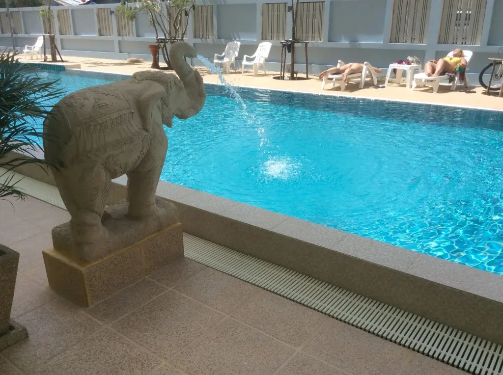 Une piscine rectangulaire avec des transats et une statue d'éléphant en pierre.