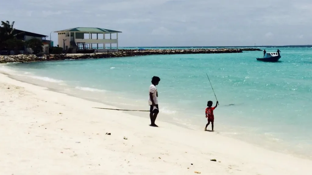 Deux personnes se tiennent sur une plage de sable blanc face à une eau turquoise.