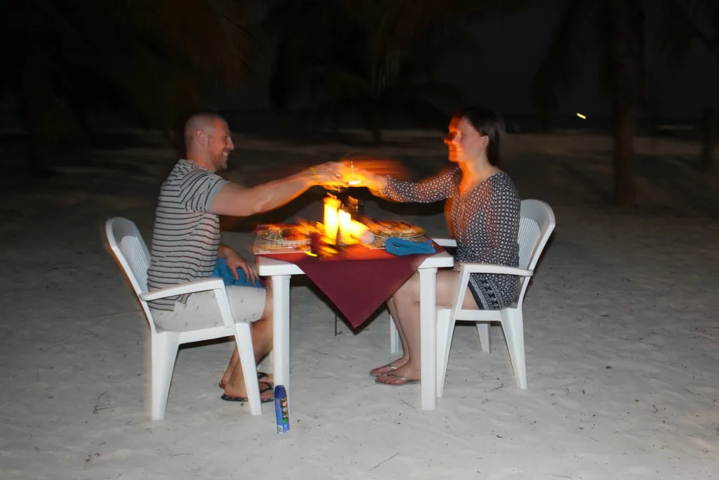 Un couple trinque avec des verres illuminés par une flamme sur une plage.