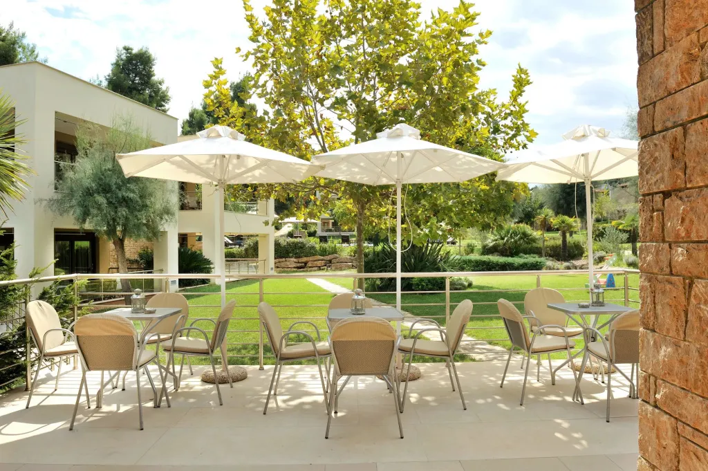 Terrasse ombragée avec tables et chaises donnant sur un jardin verdoyant.