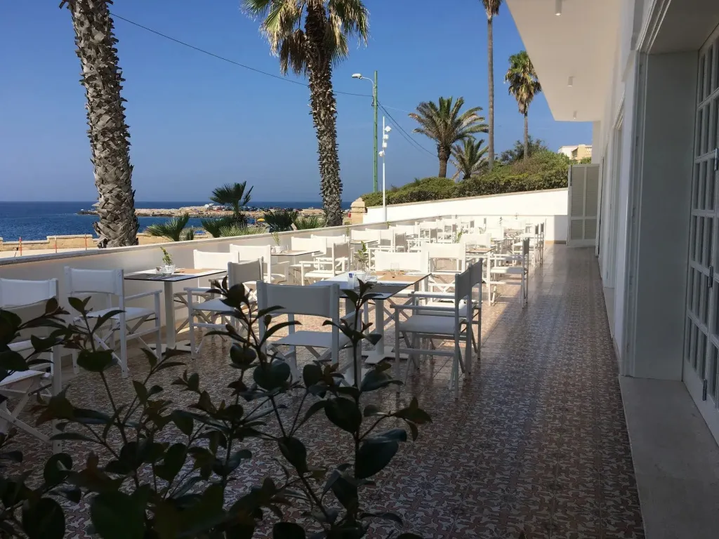 Terrasse ombragée avec tables et chaises donnant sur la mer.