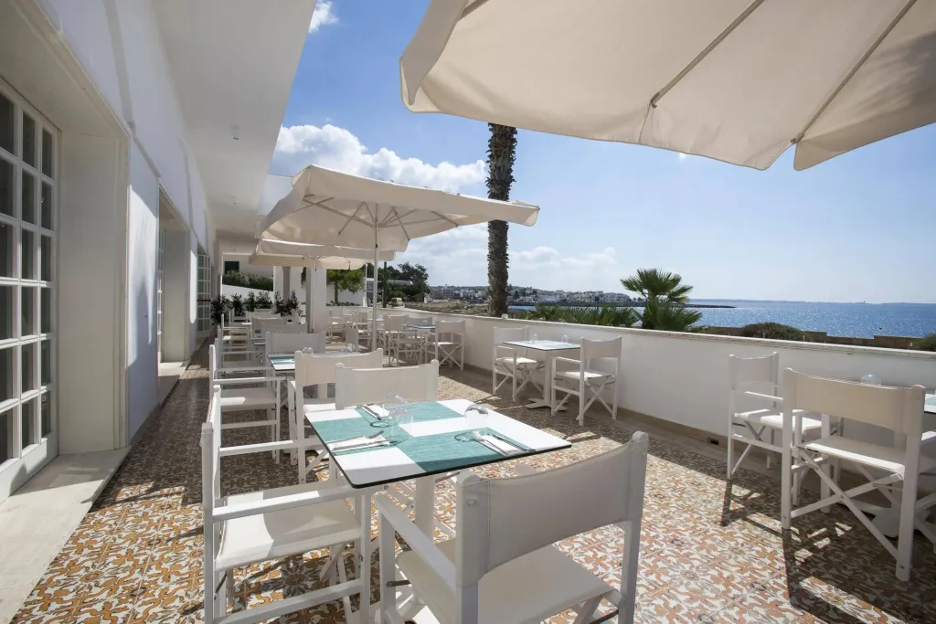 Terrasse ombragée avec tables dressées face à la mer.