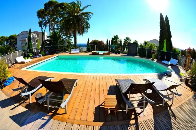 Transats et piscine ensoleillée avec végétation luxuriante en arrière-plan.