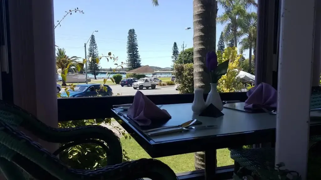 Une table est mise avec des couverts et des fleurs, donnant sur une rue et un plan d'eau.