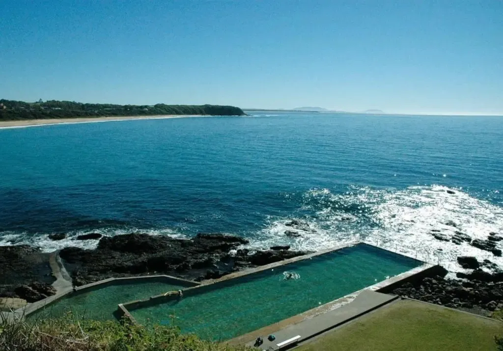 Une piscine naturelle bordée de rochers noirs surplombe la mer bleue.