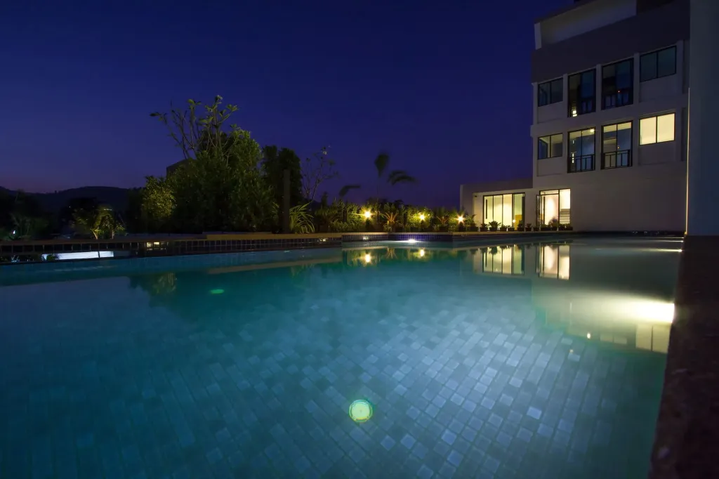 Piscine illuminée au crépuscule devant un bâtiment moderne.