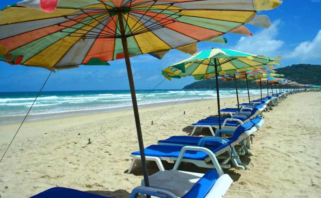 Transats bleus alignés sous des parasols colorés sur une plage de sable fin.