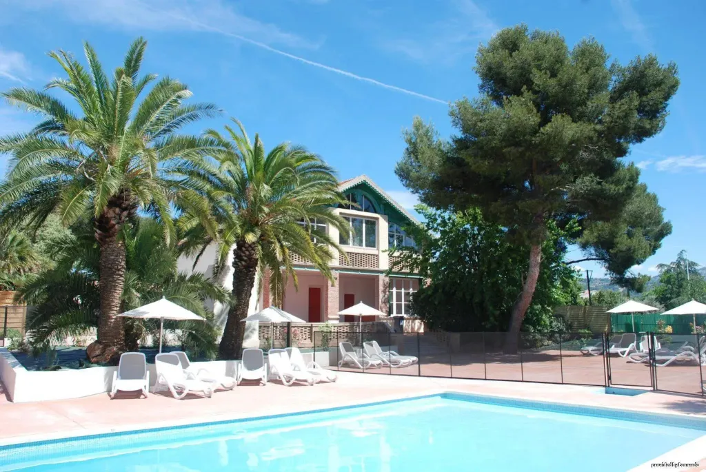 Une piscine ensoleillée avec des transats et un bâtiment à l'arrière-plan.