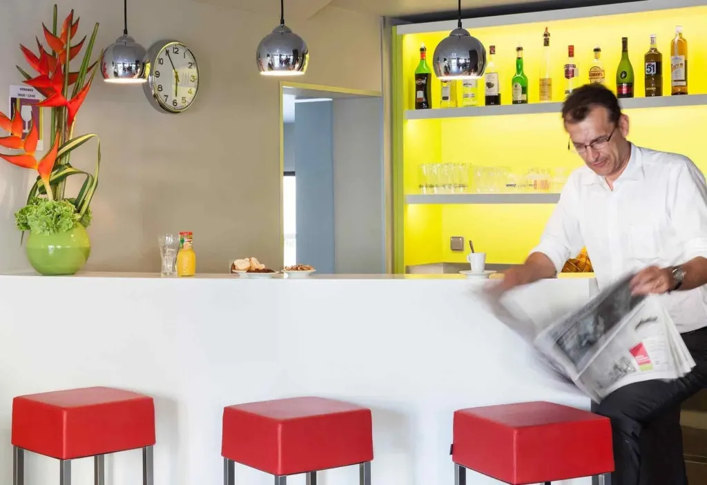 Un homme lit un journal assis au comptoir d'un bar lumineux.