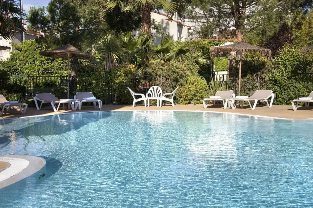 Une piscine turquoise entourée de transats et de parasols sous des palmiers.