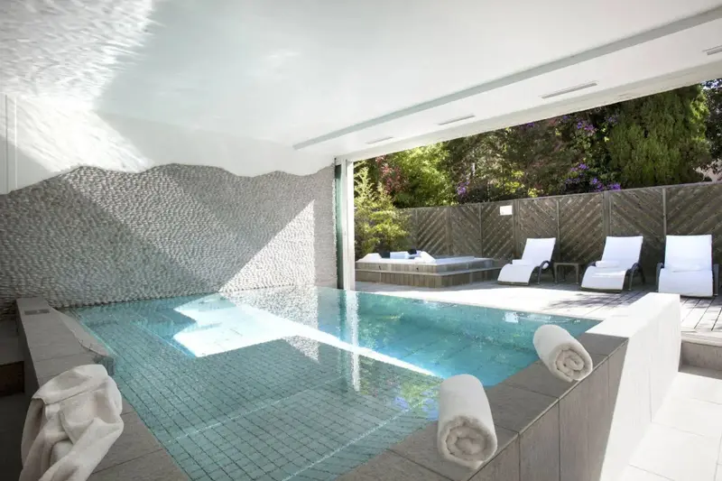 Une piscine interieure avec des transats et une vegetation luxuriante en fond.