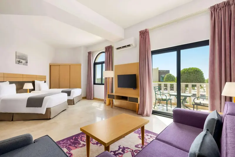 Une chambre lumineuse avec deux lits et un coin salon donnant sur une terrasse.