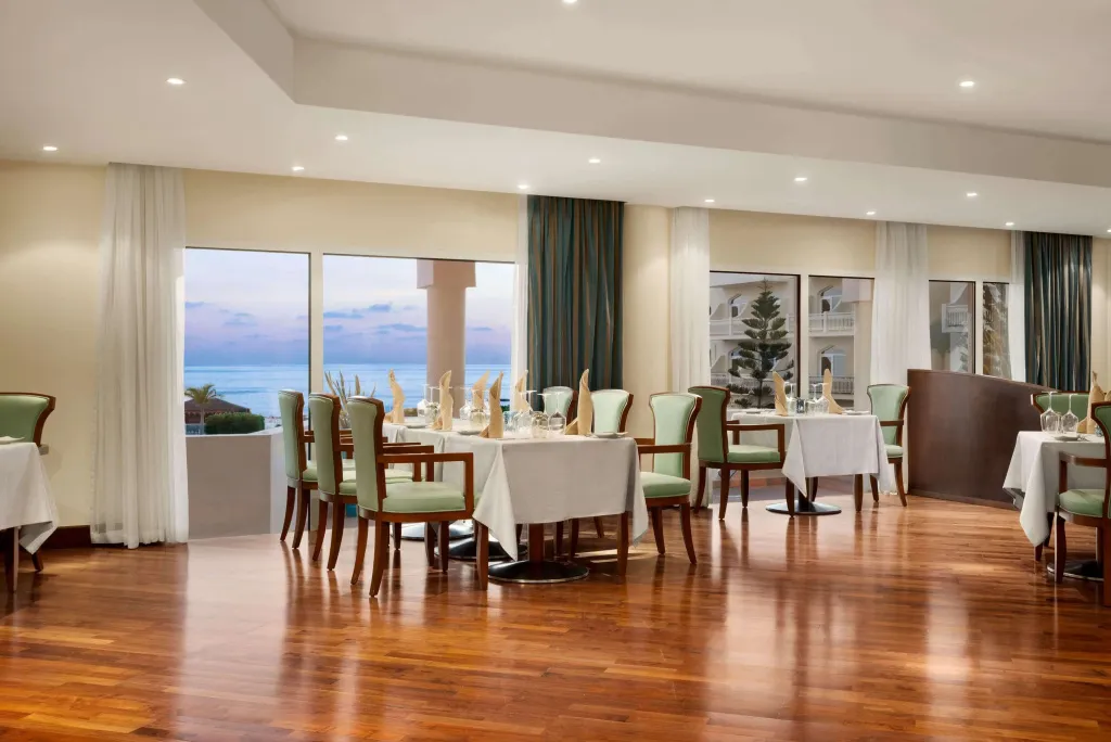 Une salle lumineuse avec des tables dressées face à une vue sur la mer.
