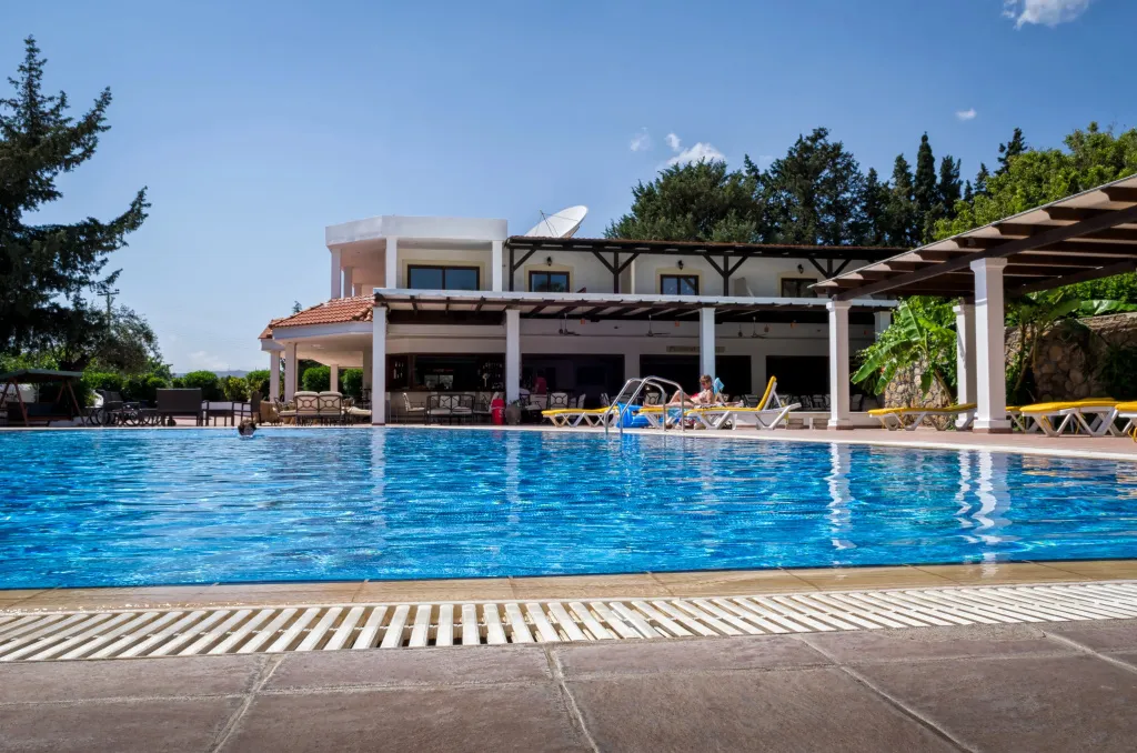 Une piscine bleue bordée d'une terrasse avec des transats et un espace ombragé.