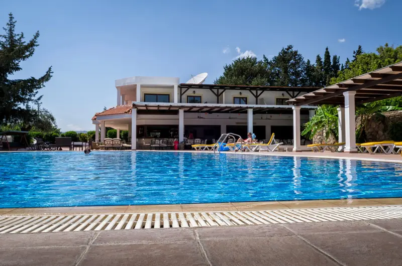 Une piscine bleue bordée d'une terrasse avec des transats et un espace ombragé.
