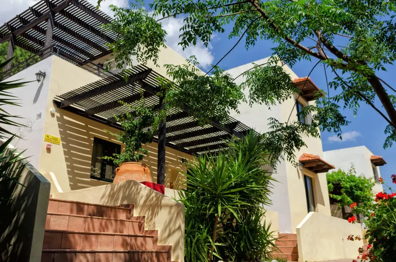 Une construction beige avec une pergola ombragée et des escaliers en pierre.