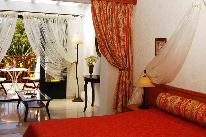 Une chambre lumineuse avec un lit rouge et un balcon fleuri.