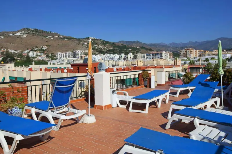 Terrasse ensoleillée avec chaises longues et vue sur la ville et les montagnes.