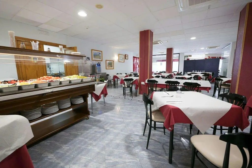 Une salle lumineuse avec un buffet garni et des tables dressées pour le repas.