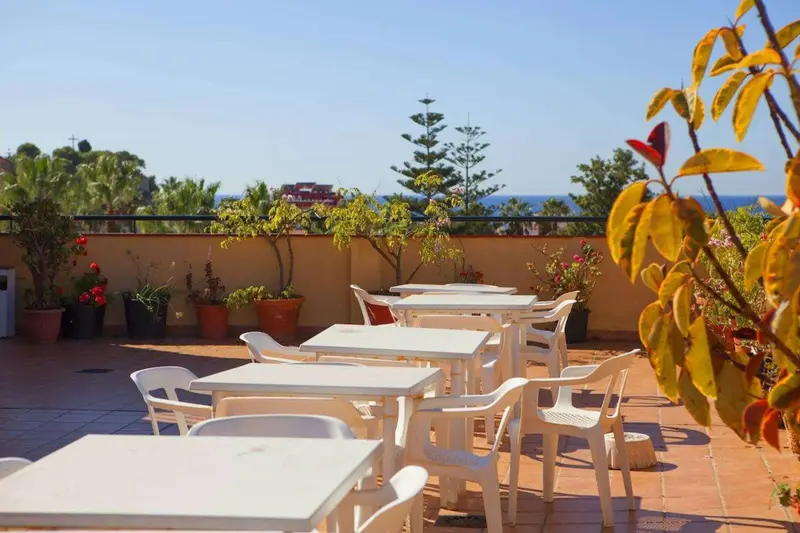 Terrasse aménagée avec tables et chaises, offrant une vue sur la mer et la végétation.