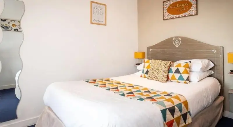Une chambre lumineuse avec un lit double décoré de coussins colorés et d'une couverture à motifs géométriques.