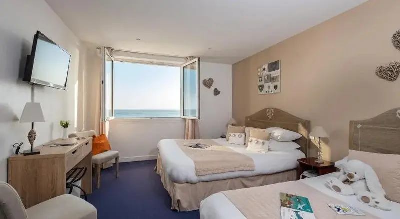 Une chambre lumineuse avec vue sur la mer par de grandes fenêtres ouvertes.