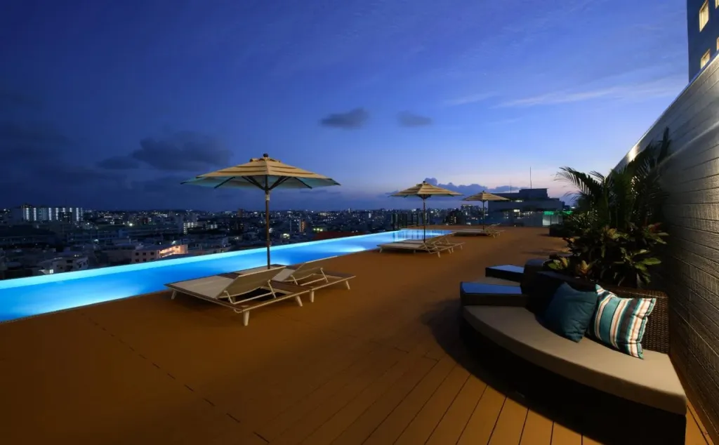 Terrasse avec piscine à débordement et vue sur la ville illuminée au crépuscule.