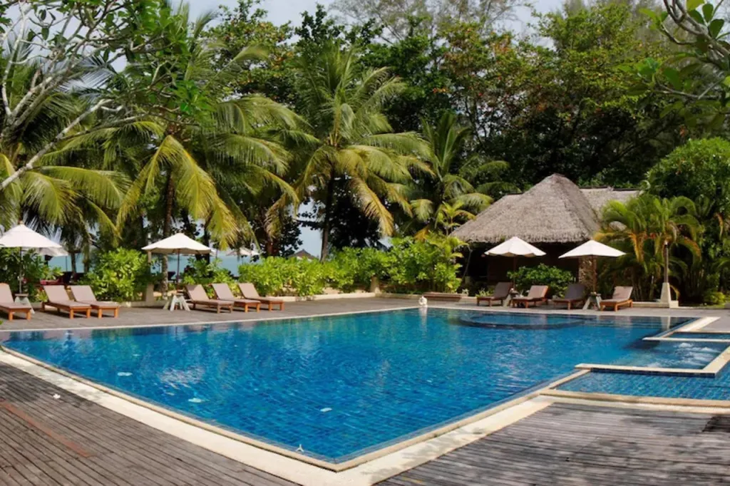 Une piscine bleue bordée de transats et de parasols, entourée d'une végétation luxuriante.