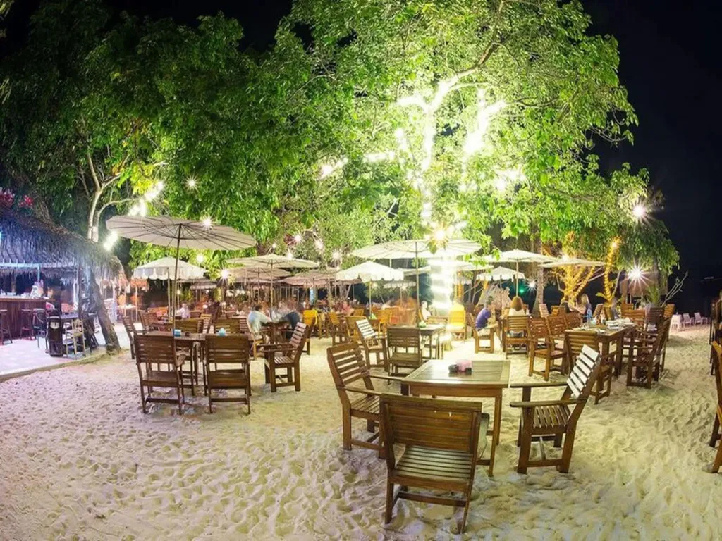 Tables et chaises disposées sur une plage éclairée la nuit.