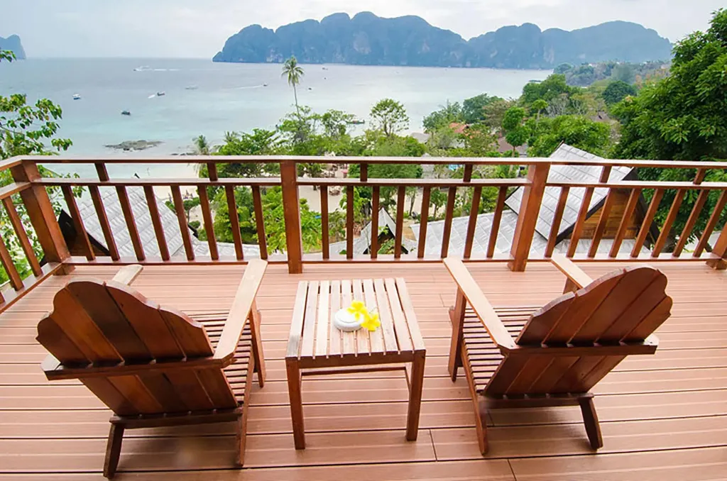 Terrasse en bois avec deux fauteuils et une petite table basse offrant une vue sur la mer et la végétation.