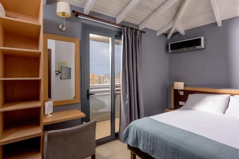 Une chambre lumineuse avec un lit et un espace bureau près d'une baie vitrée.