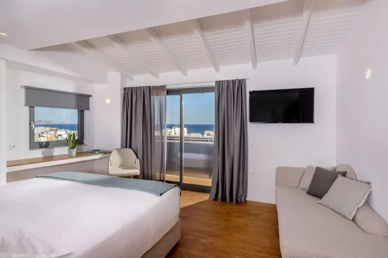 Une chambre lumineuse avec un lit et un canapé donnant sur une vue urbaine et maritime.
