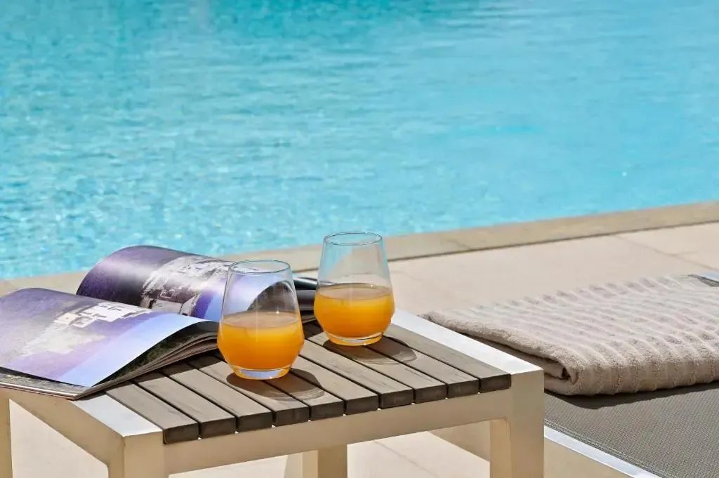 Deux verres de jus d'orange et un magazine reposent sur une table basse au bord d'une piscine.