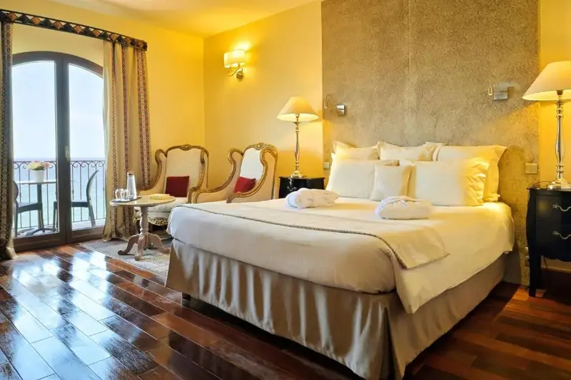 Une chambre lumineuse avec un grand lit et un balcon donnant sur la mer.