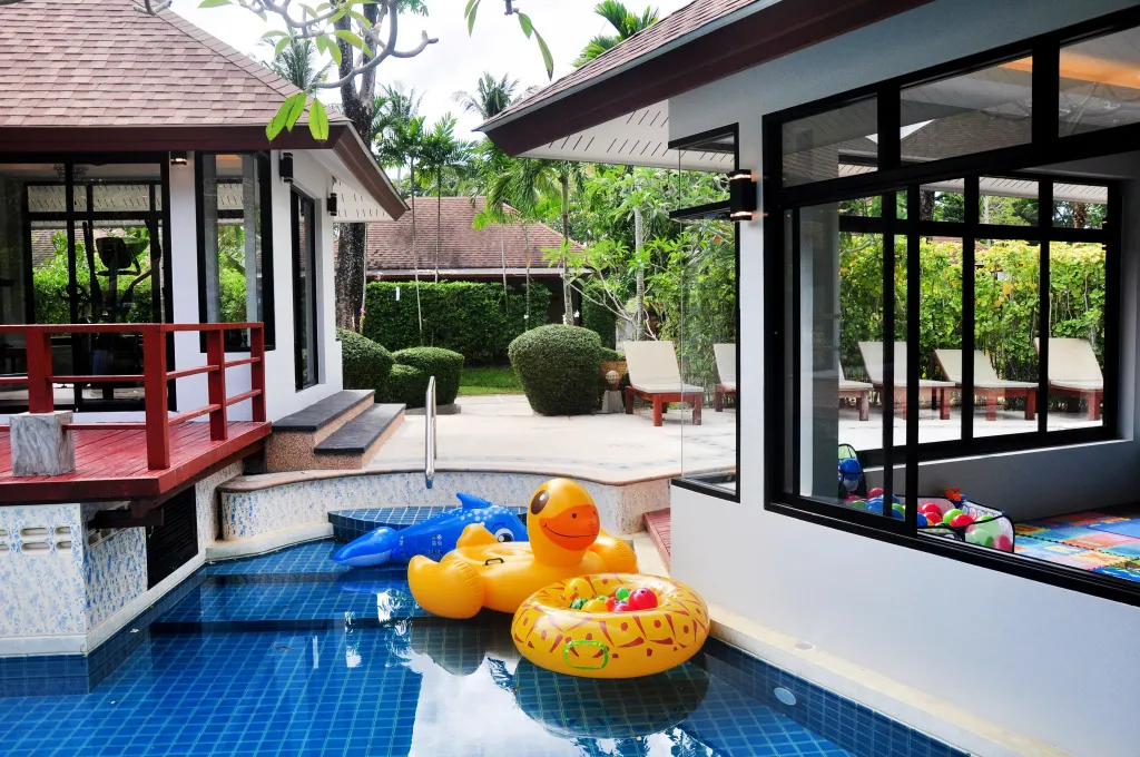 Une piscine avec des bouées colorées au premier plan et des transats sur une terrasse en arrière-plan.
