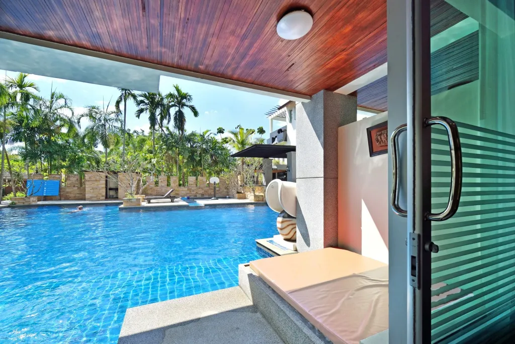 Une terrasse ombragée donne sur une piscine bleue bordée de végétation.
