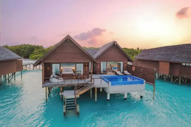 Maisons sur pilotis avec piscine privée au coucher du soleil.