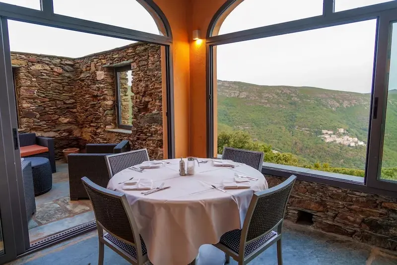 Une table ronde dressée dans une salle lumineuse avec vue sur un paysage montagneux.