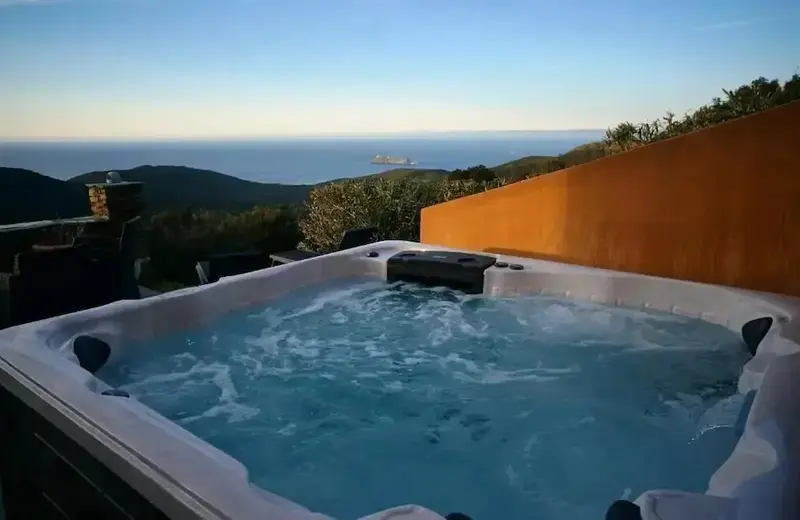Un jacuzzi extérieur offre une vue dégagée sur la mer et les collines environnantes.