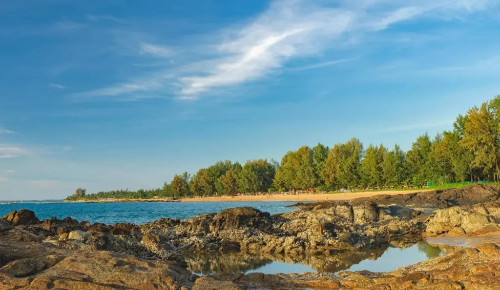 Cote rocheuse bordant une plage de sable fin sous un ciel nuageux.