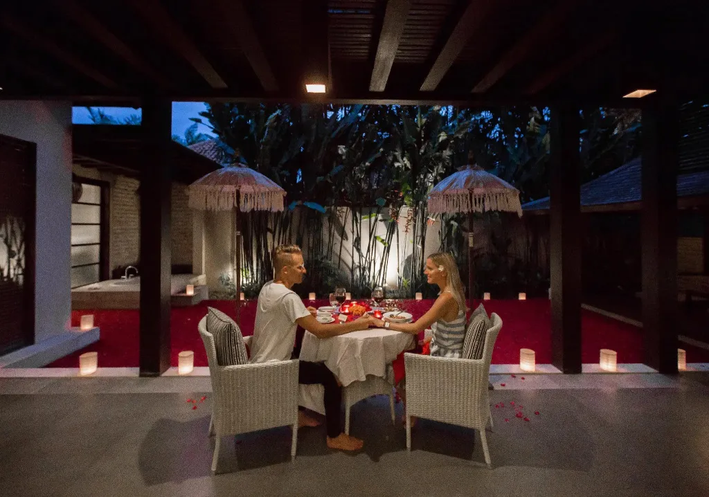 Un couple dîne à une table éclairée aux chandelles dans une cour ombragée.