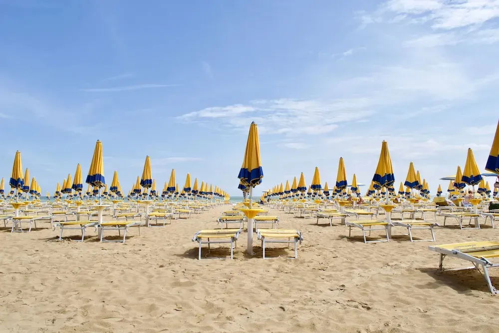Plage de sable avec transats et parasols jaunes et bleus sous un ciel clair.